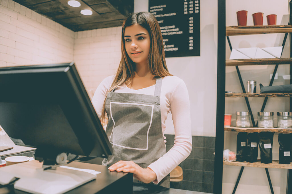 A beautiful café worker standing behind an EPOS system, ready to take an order from a customer.