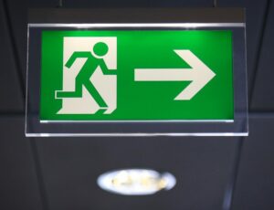 A green emergency exit sign hangs from the ceiling, featuring a white figure running through a door and an arrow pointing to the right, clearly guiding customers towards safety.