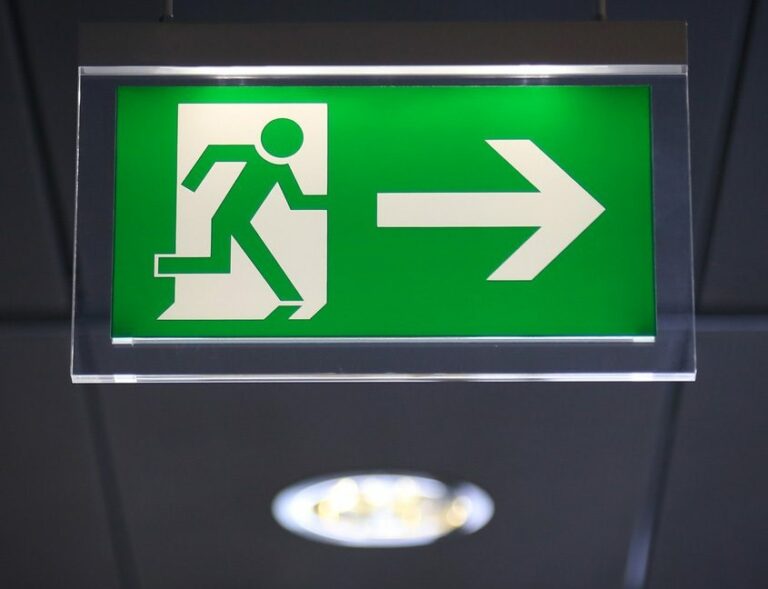 A green emergency exit sign hangs from the ceiling, featuring a white figure running through a door and an arrow pointing to the right, clearly guiding customers towards safety.