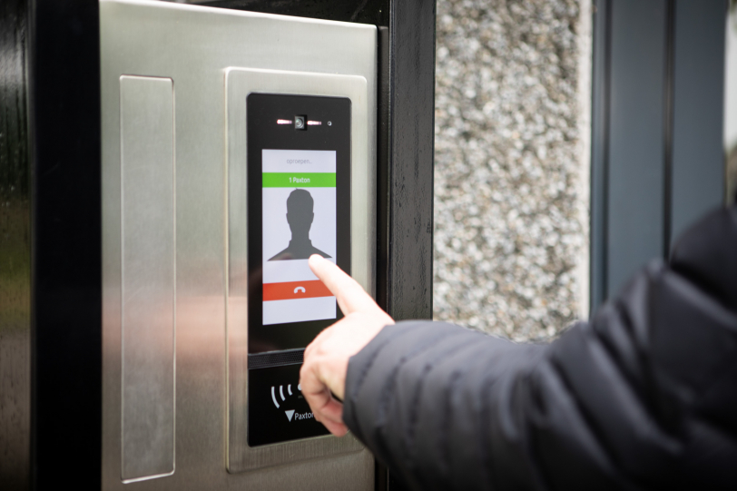 A person interacts with a CCR Systems touchscreen intercom. The screen displays options for answering or declining a call, showing a silhouette of a caller. A hand presses the screen to engage with the interface seamlessly.