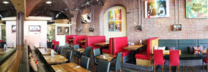 A cosy restaurant interior with exposed brick walls and red and black seating sets the stage for a culinary success story. Colourful pop art pieces adorn the walls, as tables are elegantly set with glassware and serviettes. The high ceilings and ambient lighting add to the charm.