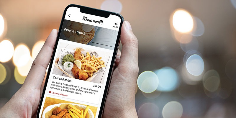 An individual holds a smartphone displaying the menu for The Flying Hog, supported by EPOS software, featuring the dish option Cod and chips priced at £6.99. The background is a dreamy blur with circular lights.
