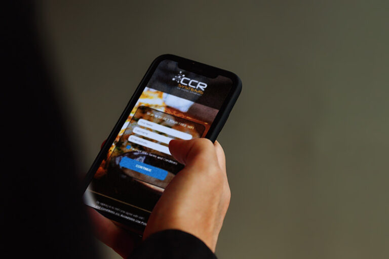 A person holds a mobile phone showing a login screen for an app with fields for username and password, connecting to Wi-Fi. The background is blurred.