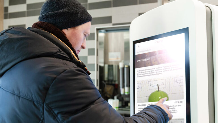 A man near self service restaurant, kiosk, terminal with empty screen.