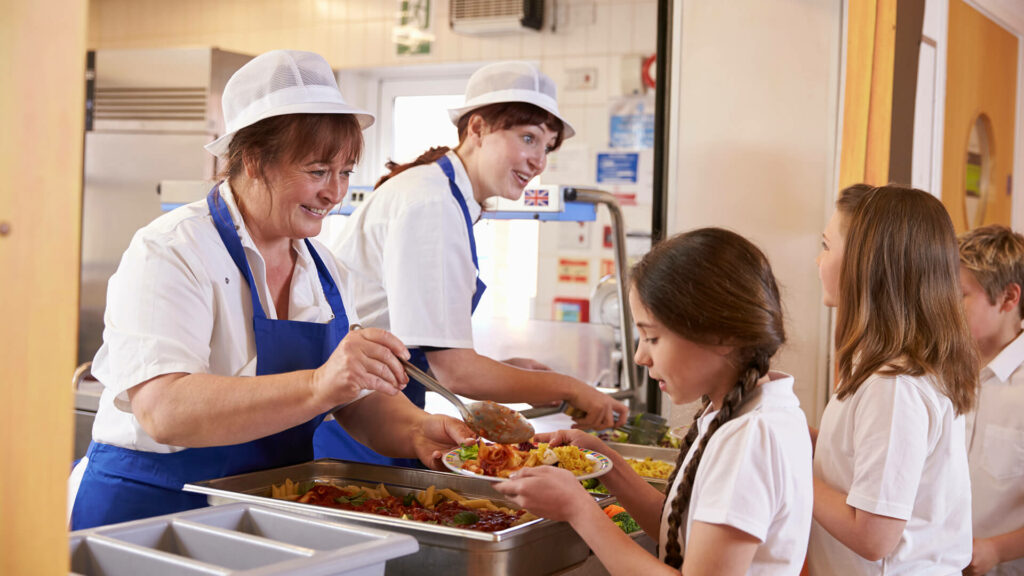Two dinner ladies serving school kids lunch