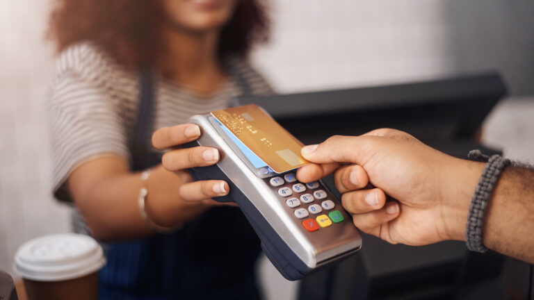 A customer taps a contactless payment card onto a handheld card terminal, a transaction subject to merchant service charges.